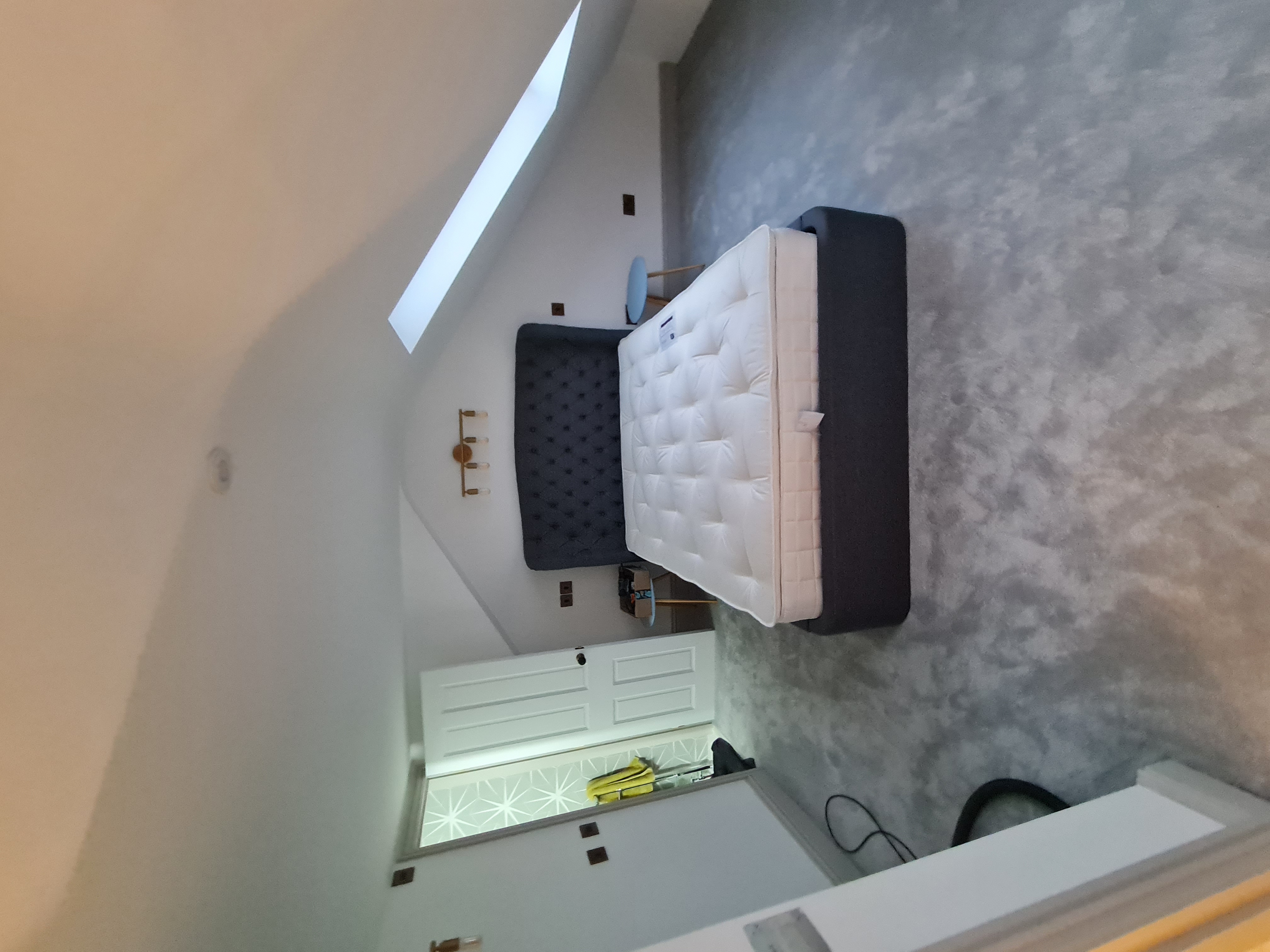 Loft bedroom with Velux skylight, navy upholstered bed and grey carpet