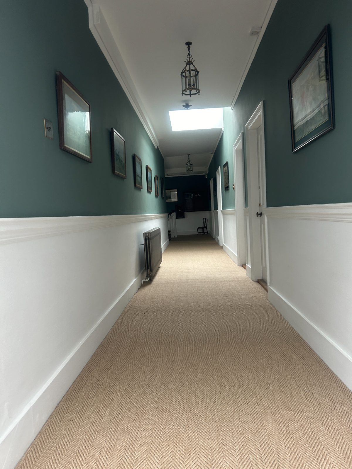 Period manor hallway with deep green walls, white dado panelling and framed art