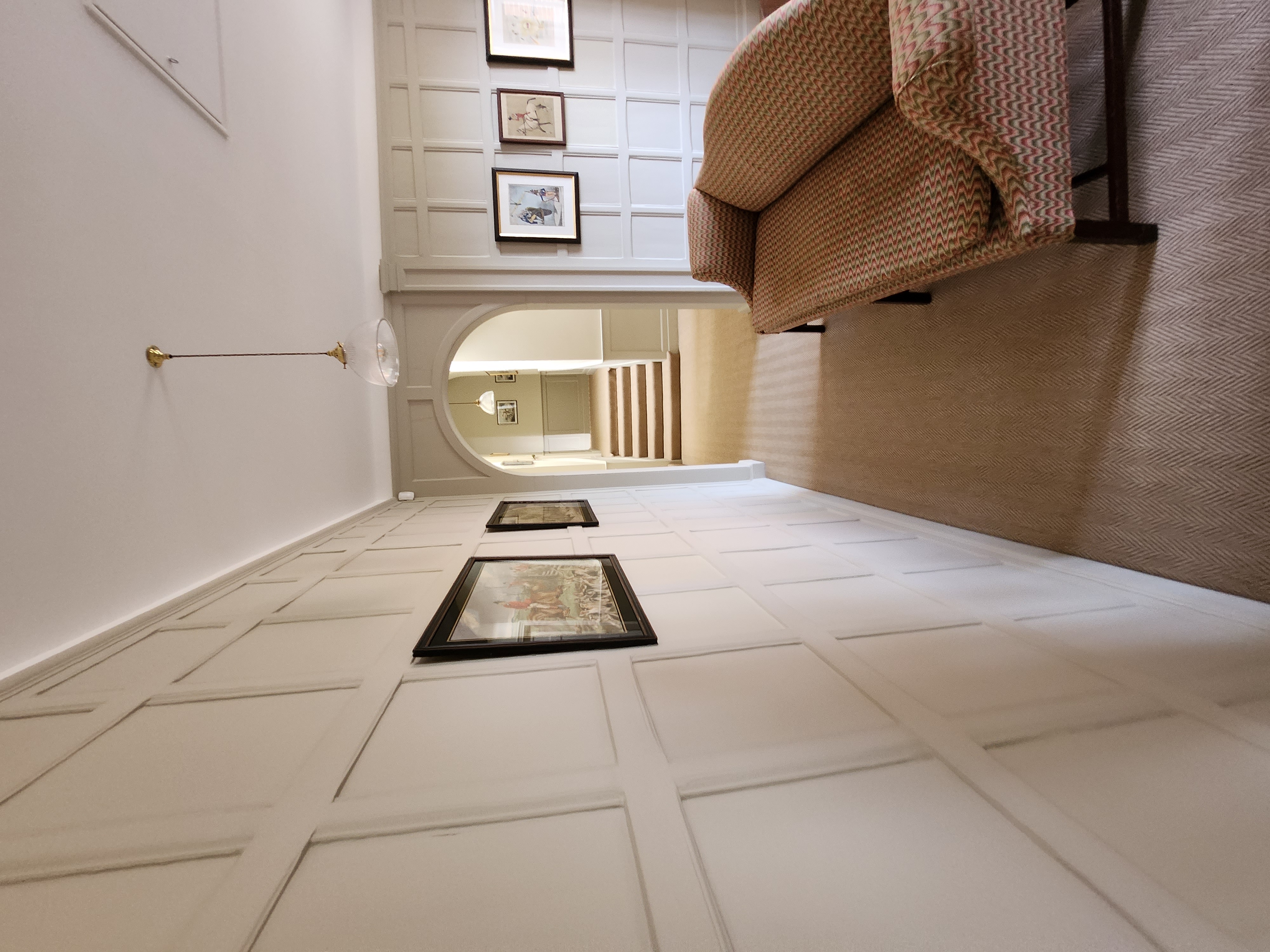 Panelled country hallway with arch opening, framed prints and herringbone carpet