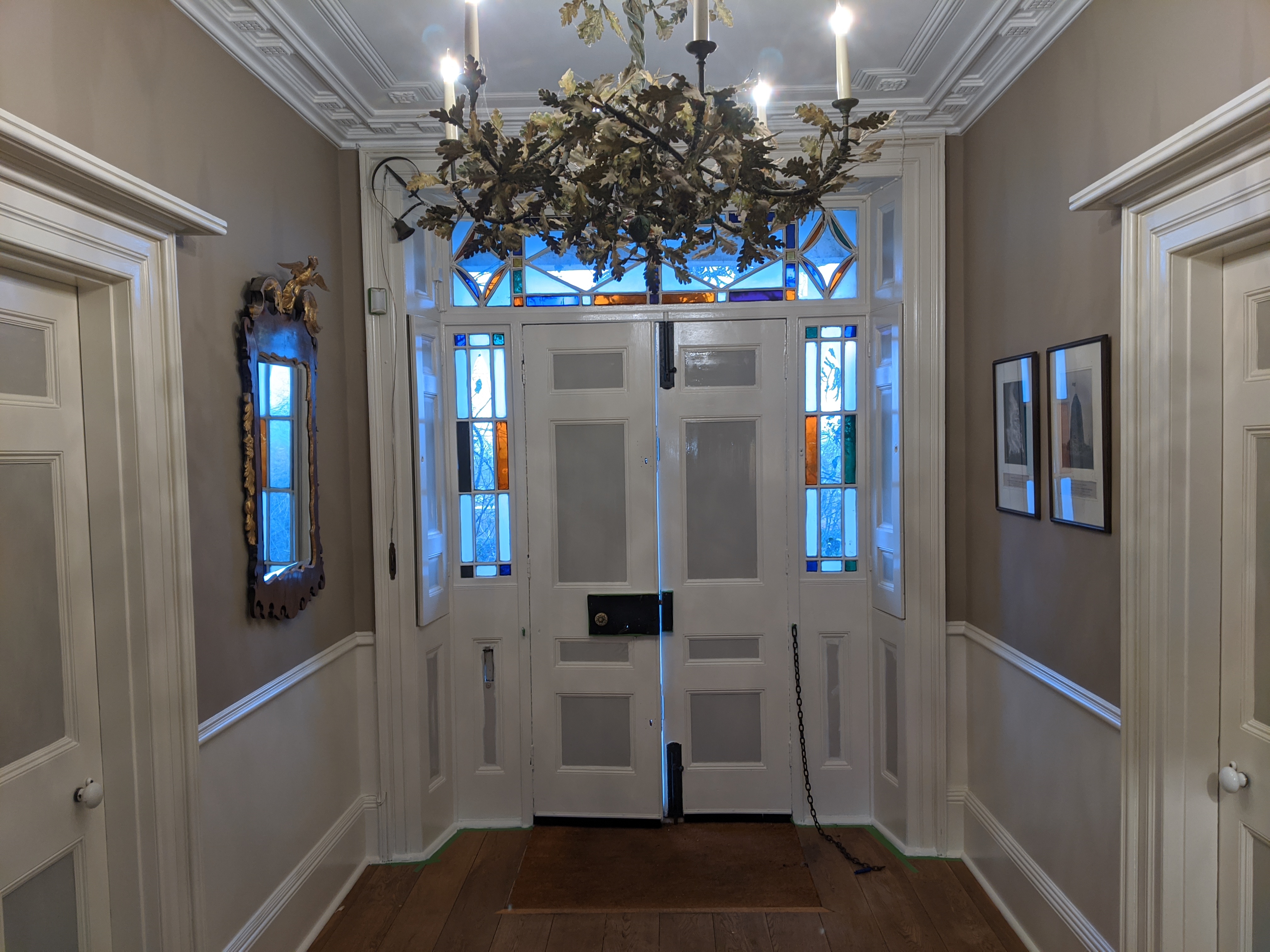 Grand entrance hallway with stained glass door, chandelier and taupe panelled walls