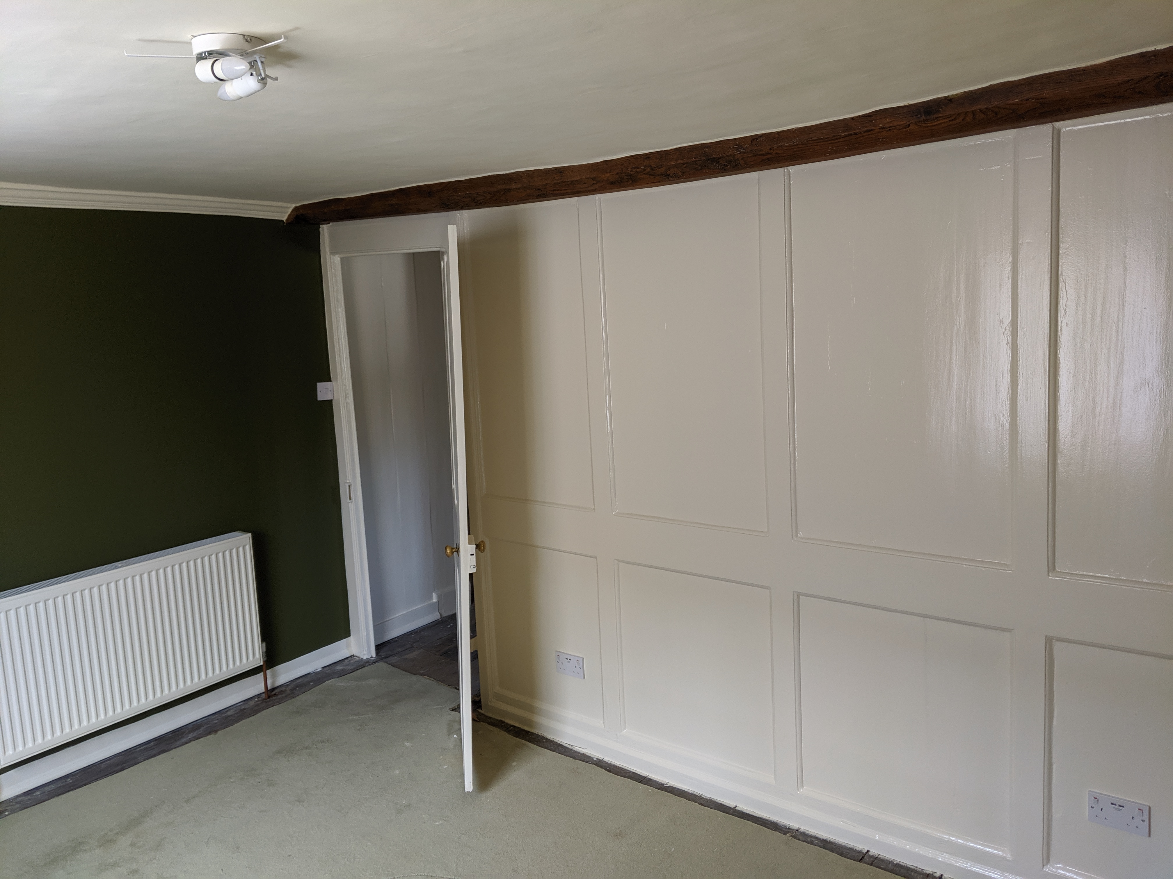 Room with olive green wall, cream painted panelling and exposed ceiling beam