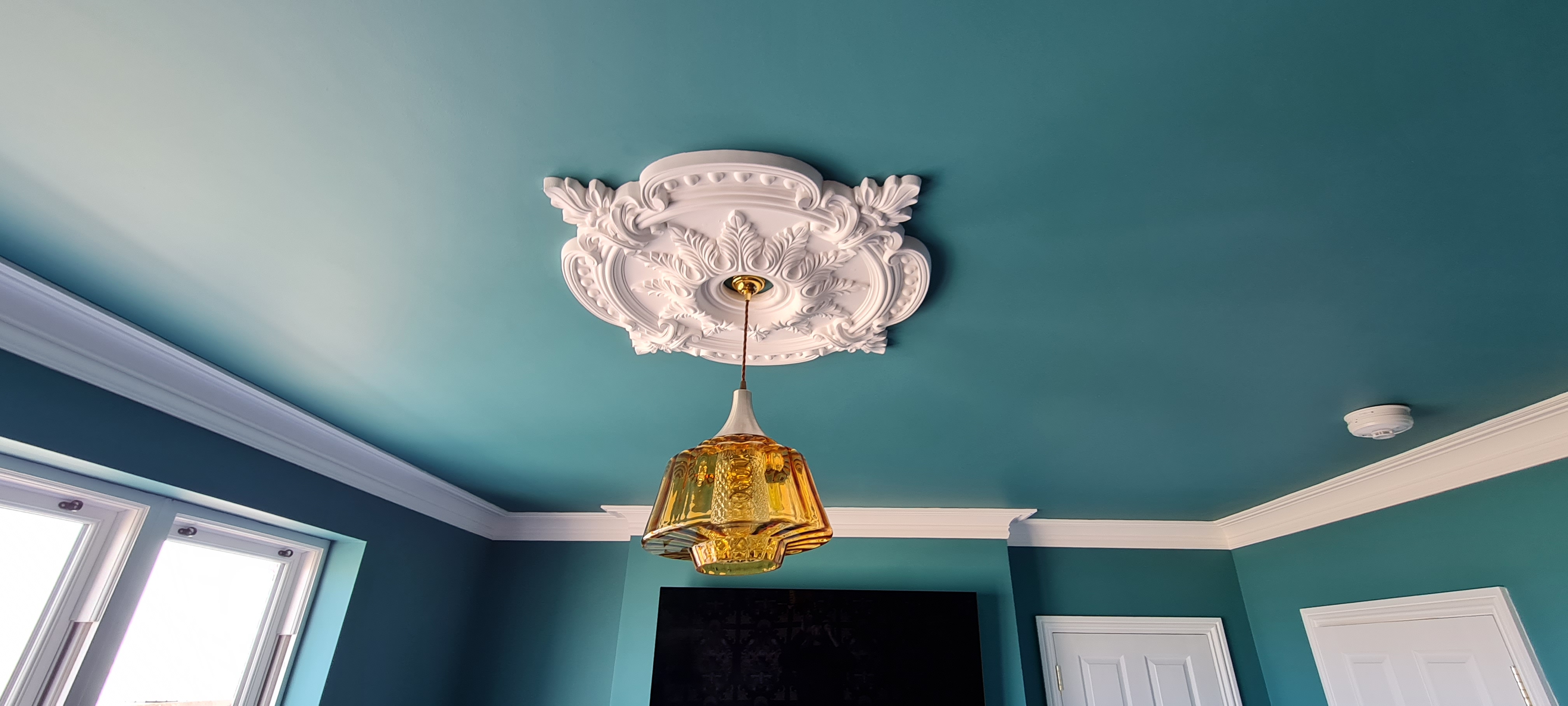 Ornate plaster ceiling rose against deep teal painted ceiling with amber pendant