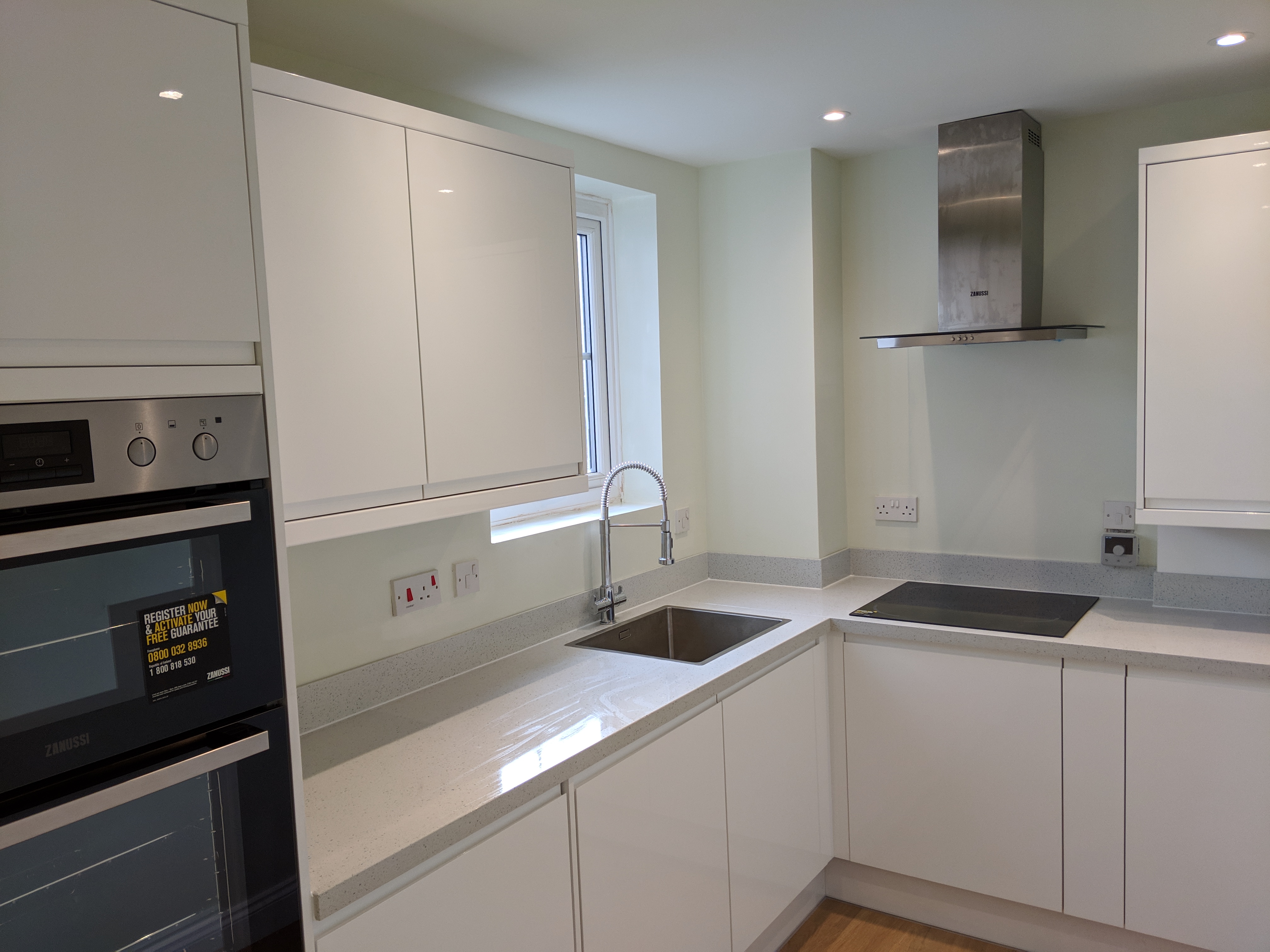 Modern kitchen with gloss white units, sage green walls and recessed spotlights