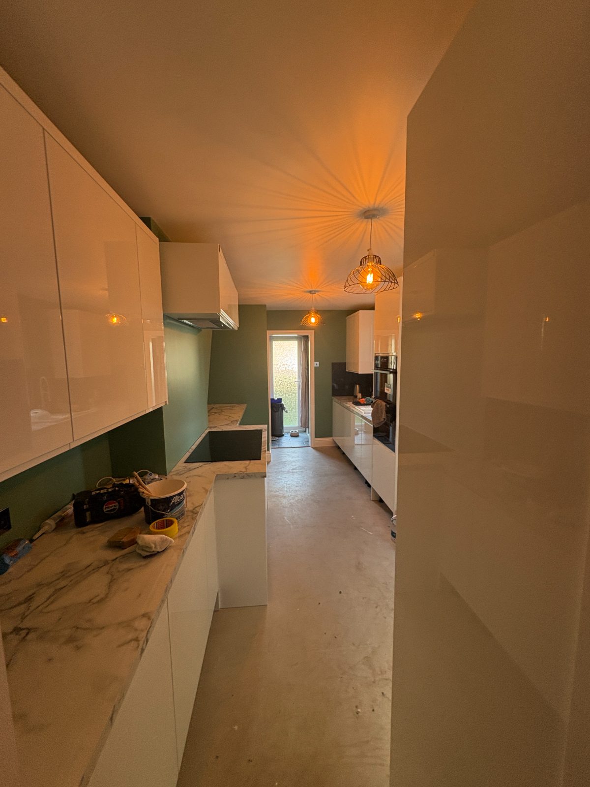 Cream gloss fitted kitchen with a sage green feature wall