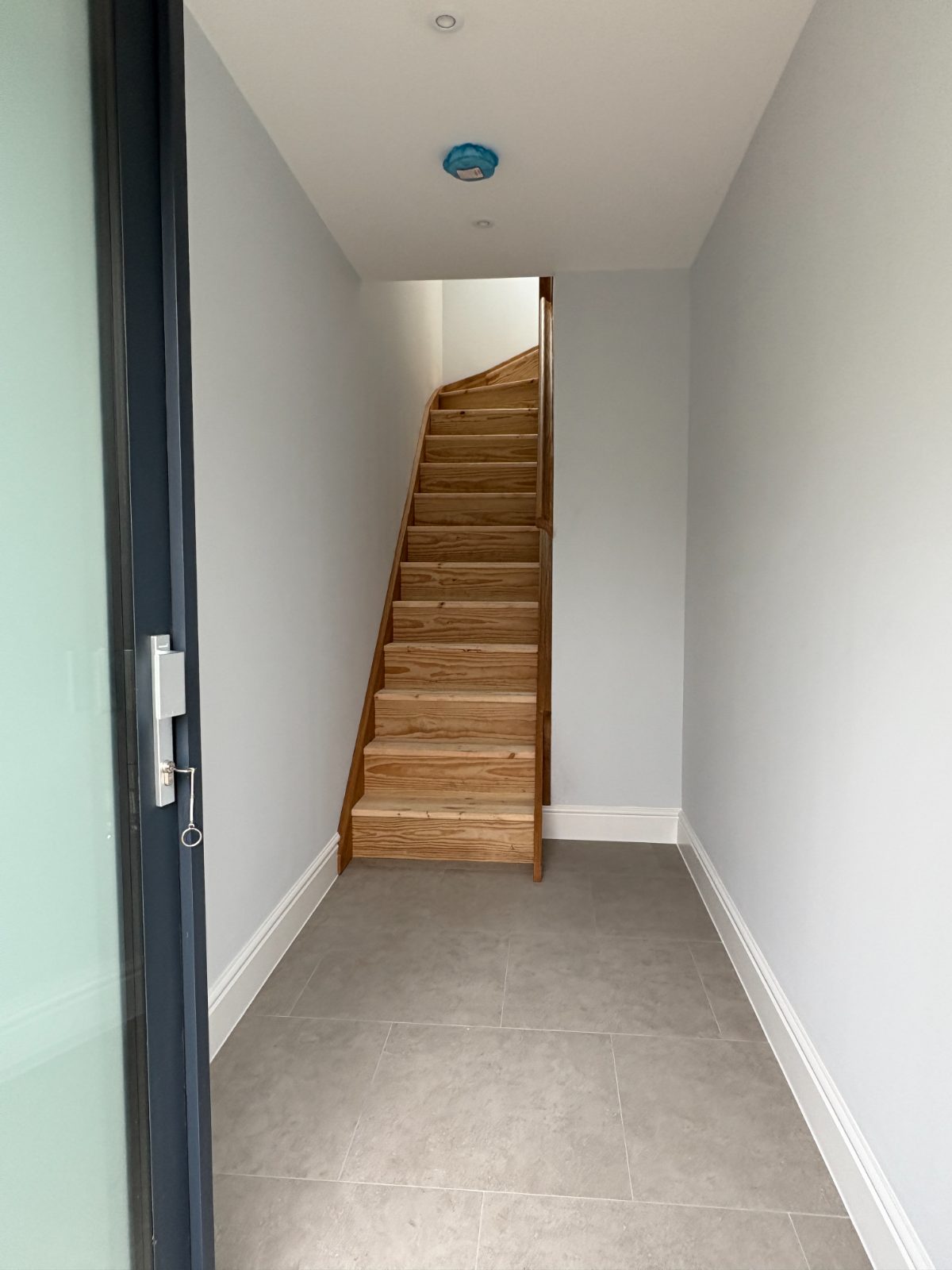 Wooden staircase with white walls beside a tiled hallway