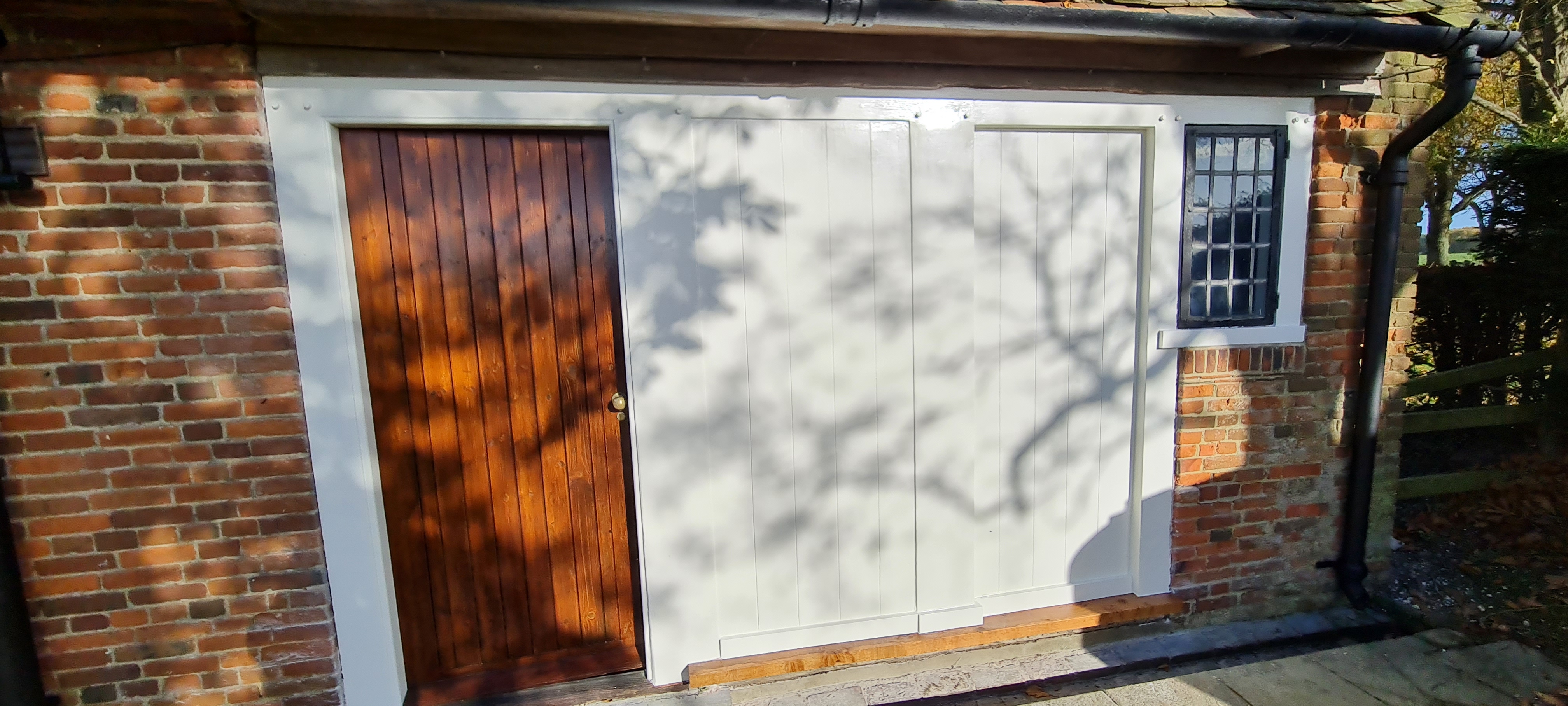 Country outbuilding after painting — white garage doors and oiled timber side door