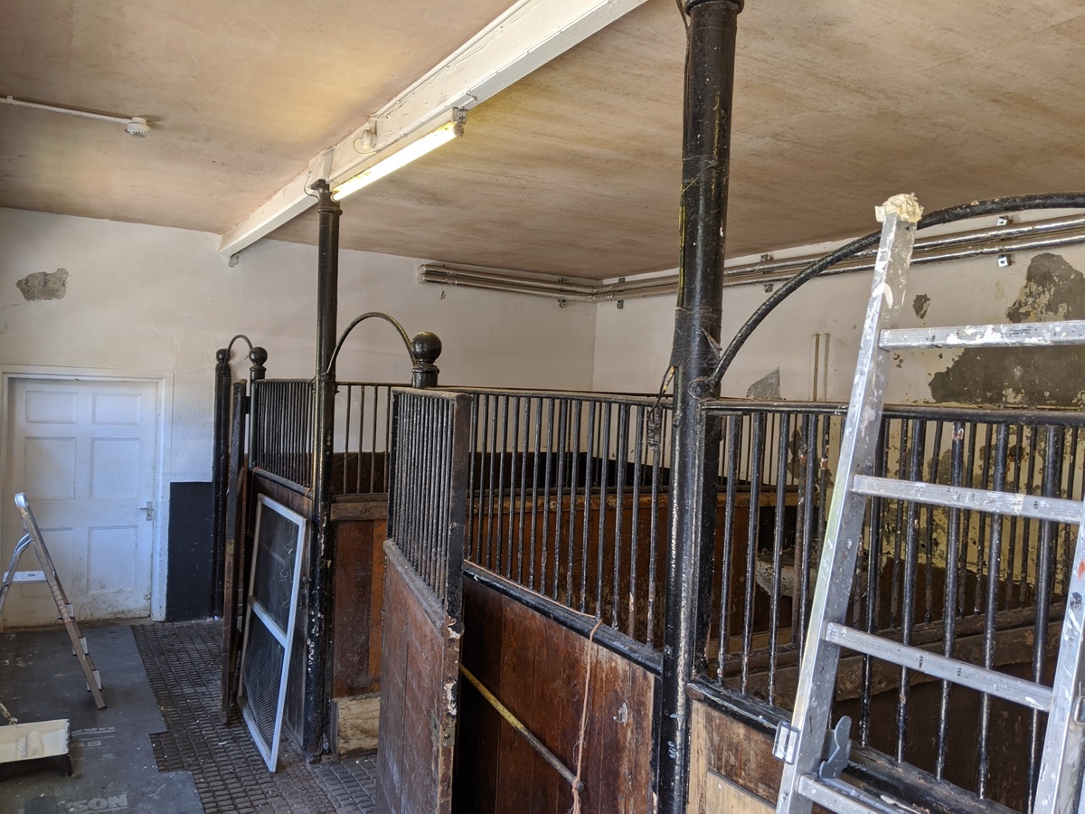 Estate stables before restoration — tired timber, peeling paint and a cluttered floor
